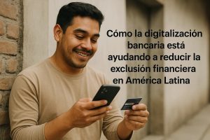 Hombre sonriente sostiene un teléfono móvil y una tarjeta de crédito frente a una pared de ladrillos, con el texto “Cómo la digitalización bancaria está ayudando a reducir la exclusión financiera en América Latina”, representando la expansión de los servicios financieros digitales en América Latina.
